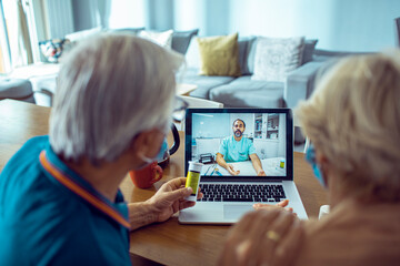 Senior couple wearing face masks having video call with doctor about medication with laptop at home