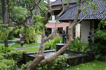 Fototapeta premium Traditional Balinese style garden with tropical plants, stone Balinese statues, and a decorative pond. Perfect for nature-inspired outdoor decor and tropical landscaping.