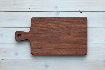 Handmade walnut wood chopping board on light blue wooden table. wooden board on wooden background