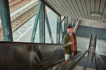 Mature man using a smart phone while going up the escalator at a train station