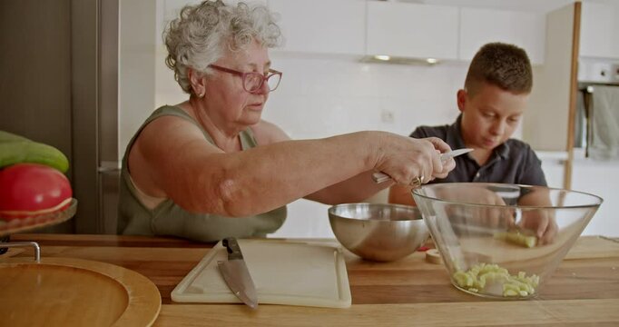 Heartwarming scene of family connection as a grandmother and her grandson work together to chop vegetables in a modern kitchen.