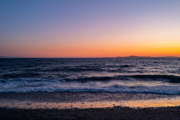 A beautiful west coast sunset on a beach on Deception Bay in Washington State with beautiful dark and smooth beach stones on the shore