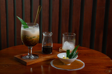 Es Cendol, a traditional indonesian beverage made with coconut milk, added with palm sugar syrup and pandan-flavored green rice flour jelly, served cold with ice cubes. Served on wooden table 