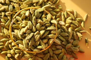 Cardamom pods in a bowl surrounded by loose pods on a table