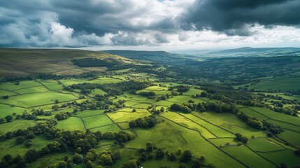 Obraz premium Aerial View of Lush Green Fields and Rolling Hills Under Dramatic Cloudy Skies in Rural Landscape.