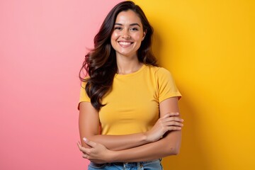 Obraz premium Cheerful Young Hispanic Woman Smiling in a Bright Yellow T-shirt Against a Vibrant Pink and Yellow Background