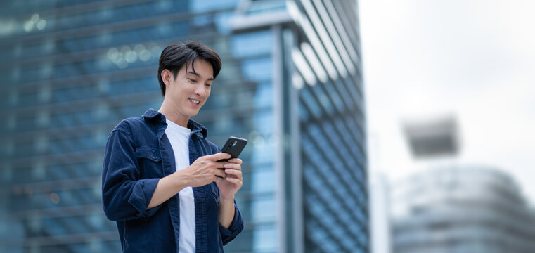 smiling happy successful asian businessman or lawyer in gray suit and blue shirt calling with his phone near his ear standing in front of an office building.Successful businessman holding mobile phone