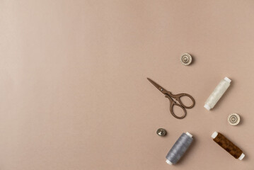 Naklejka premium Sewing accessories on beige background. Threads, scissors and buttons. Flat lay, top view. Copy space
