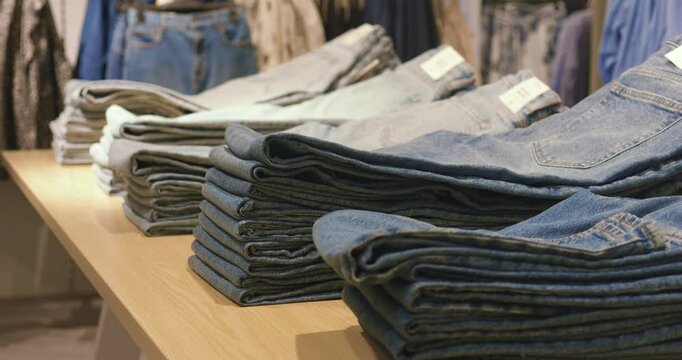 Wooden table displaying neatly folded denim jeans in multiple washes and styles, arranged for retail shopping environment
