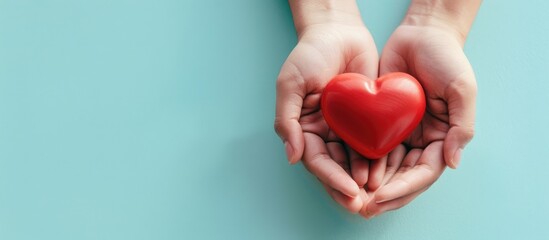 Hands holding a vibrant red heart on a soft light blue background with a clean copy space area to the left.