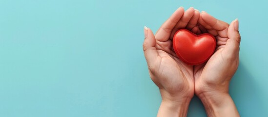 Two hands gently holding a red heart on a light blue background.