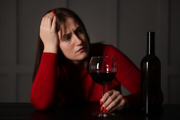 Alcohol addiction. Woman with glass of red wine and bottle at wooden table indoors