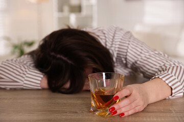 Alcohol addiction. Woman with glass of whiskey at wooden table indoors, selective focus