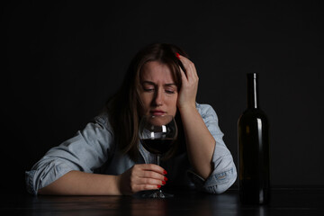 Alcohol addiction. Miserable woman with wine at table in dark