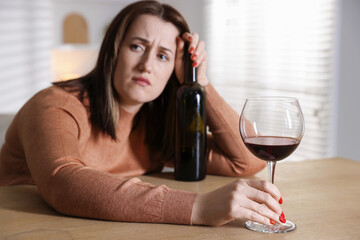 Alcohol addiction. Miserable woman with wine at table indoors, selective focus