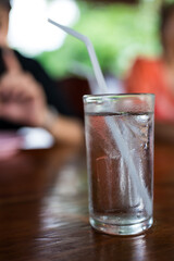 Glass of cool water with straw on a wooden table in at the restaurant with blurred background