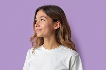Obraz premium Portrait of a Smiling Young Caucasian Woman with Long Wavy Hair Against a Soft Purple Background, Embodying Joy and Confidence in a Casual Tee