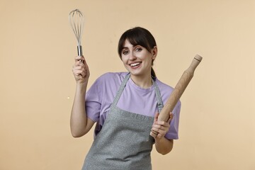 Woman with rolling pin and whisk on beige background