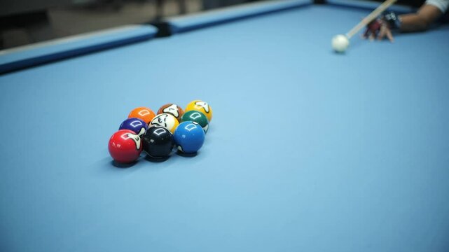 A player breaks the billiard balls on a blue pool table, sending them scattering across the surface