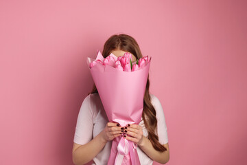 Beautiful teenage girl with bouquet of tulips on pink background