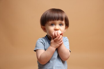 Cute little child eating tasty mochi on light brown background