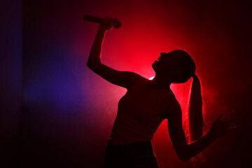 Silhouette of woman singing on dark background with color lights