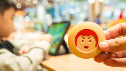 Father's hand holding red angry child symbol with background image of boy playing game on tablet. Parenting concept that too much screen time makes child have intense anger.