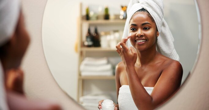 Mirror, cream and woman in bathroom, dermatology and home with cosmetics, shine and wellness. Skincare, happy person and girl with healthy skin, morning and reflection with lotion, glow and smile