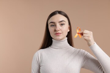 Multiple Sclerosis awareness. Young woman holding orange ribbon on beige background
