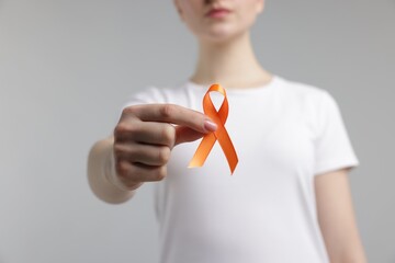 Multiple Sclerosis awareness. Young woman holding orange ribbon on light grey background, closeup
