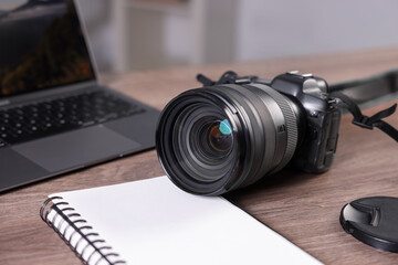 Professional photo camera, laptop and notepad on wooden desk indoors, closeup