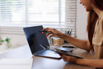 Fototapeta premium Portrait of a smiling young Asian business woman work on her desk in a large modern office working online Business Analytics with a digital tablet 