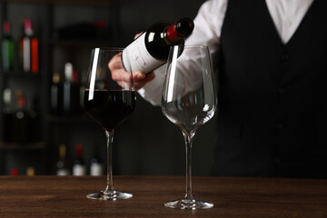 Professional sommelier pouring red wine into glasses at wooden table indoors, closeup