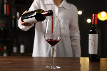 Professional sommelier pouring red wine into glass at wooden table indoors, closeup