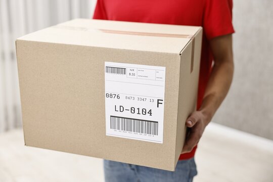 Man holding parcel with shipping label indoors, closeup