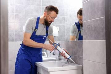 Obraz premium Worker with caulking gun sealing washbasin in bathroom