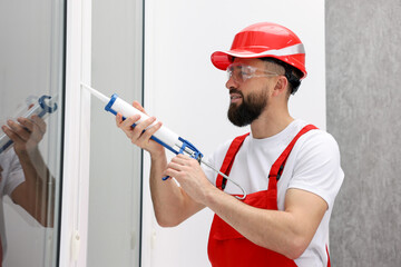 Worker with caulking gun sealing window indoors