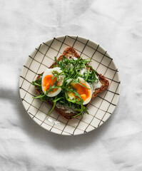 Sandwich with cream cheese, boiled egg, arugula on a light background
