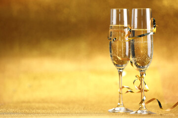 Champagne in glasses and streamers on golden background. Space for text