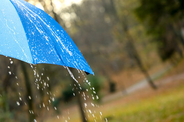 Open blue umbrella under pouring rain outdoors, closeup. Space for text