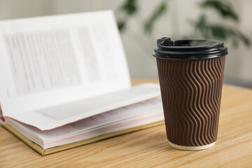 Paper cup and open book on wooden table indoors, closeup. Mockup for design