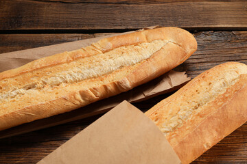 Paper bags with fresh baguettes on wooden table, closeup