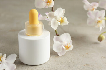 Bottle of skin care product and orchid flowers on gray textured surface