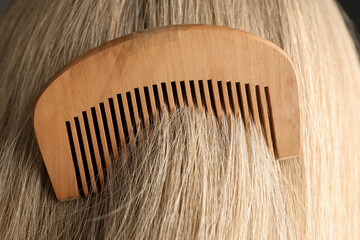 Obraz premium Brushing hair with wooden comb, closeup view