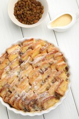 Delicious bread pudding with raisins, powdered sugar, condensed milk on white wooden table, flat lay