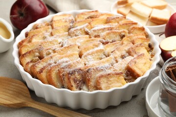 Delicious bread pudding with raisins, powdered sugar and apples on grey table, closeup