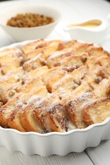 Delicious bread pudding with raisins and powdered sugar on white wooden table, closeup