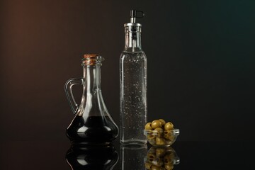 Salad dressings and olives on mirror surface against dark background