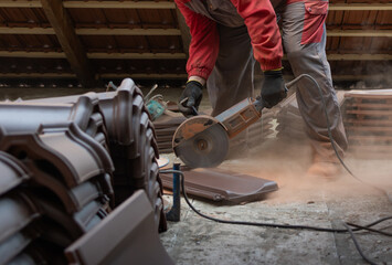 A worker cuts a red roof tile.
