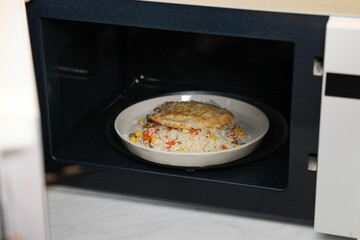 Plate with rice and meat cutlet in microwave, closeup